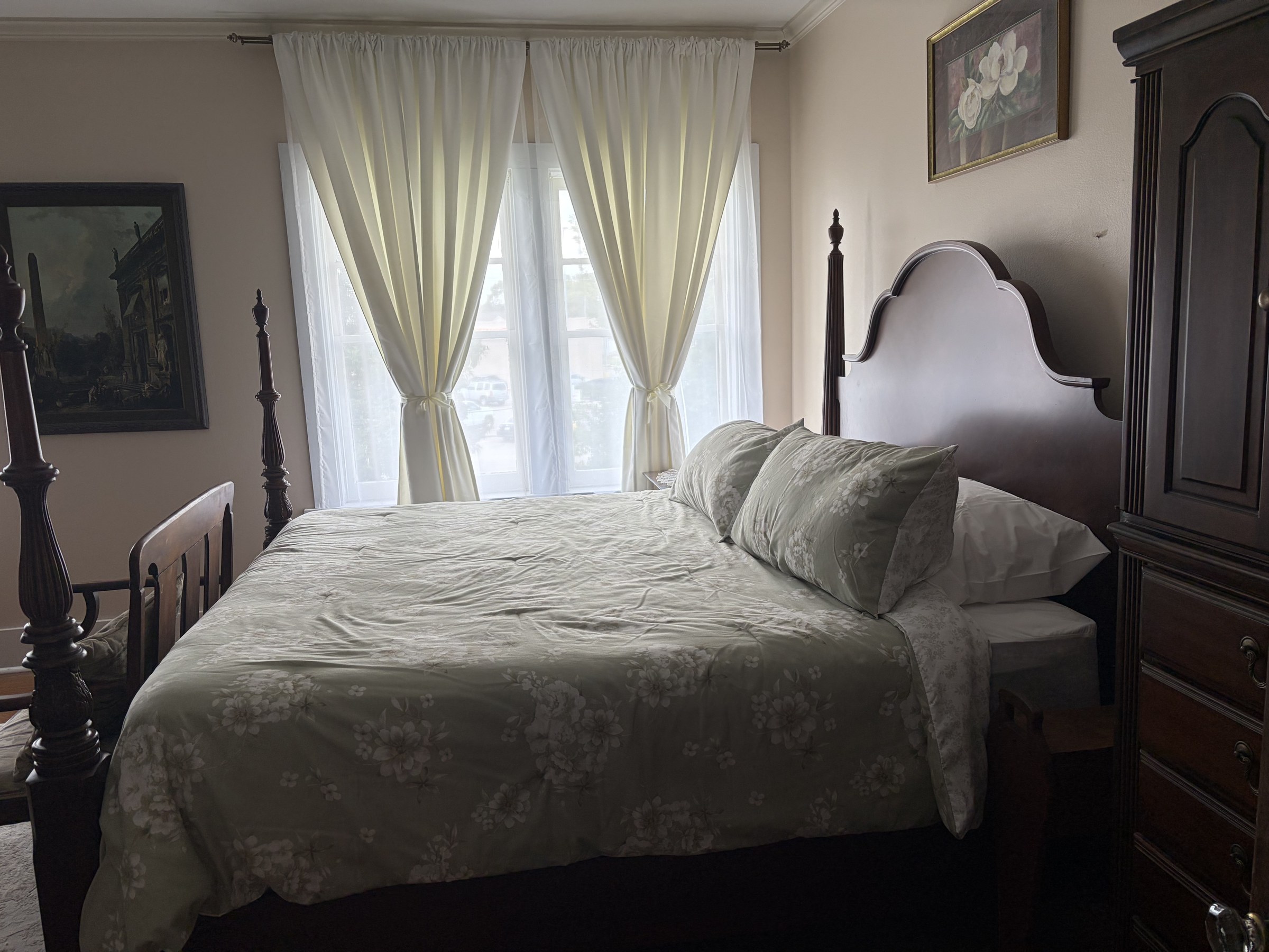Lillian: a dark wood king bed with a sage floral coverlet and cream drapes.