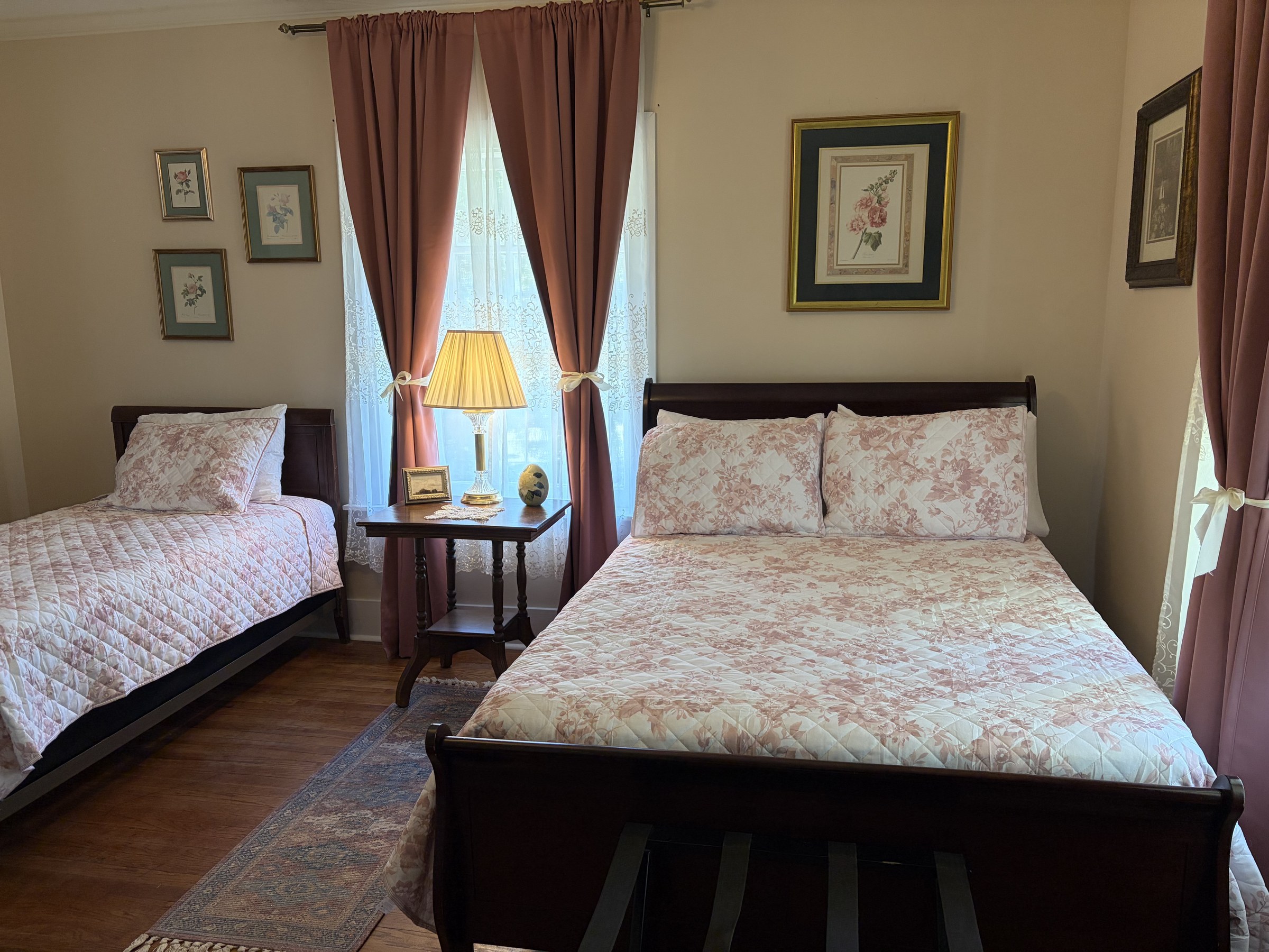 Margaret: two dark wood sleigh beds with rose floral quilts and a window between them.