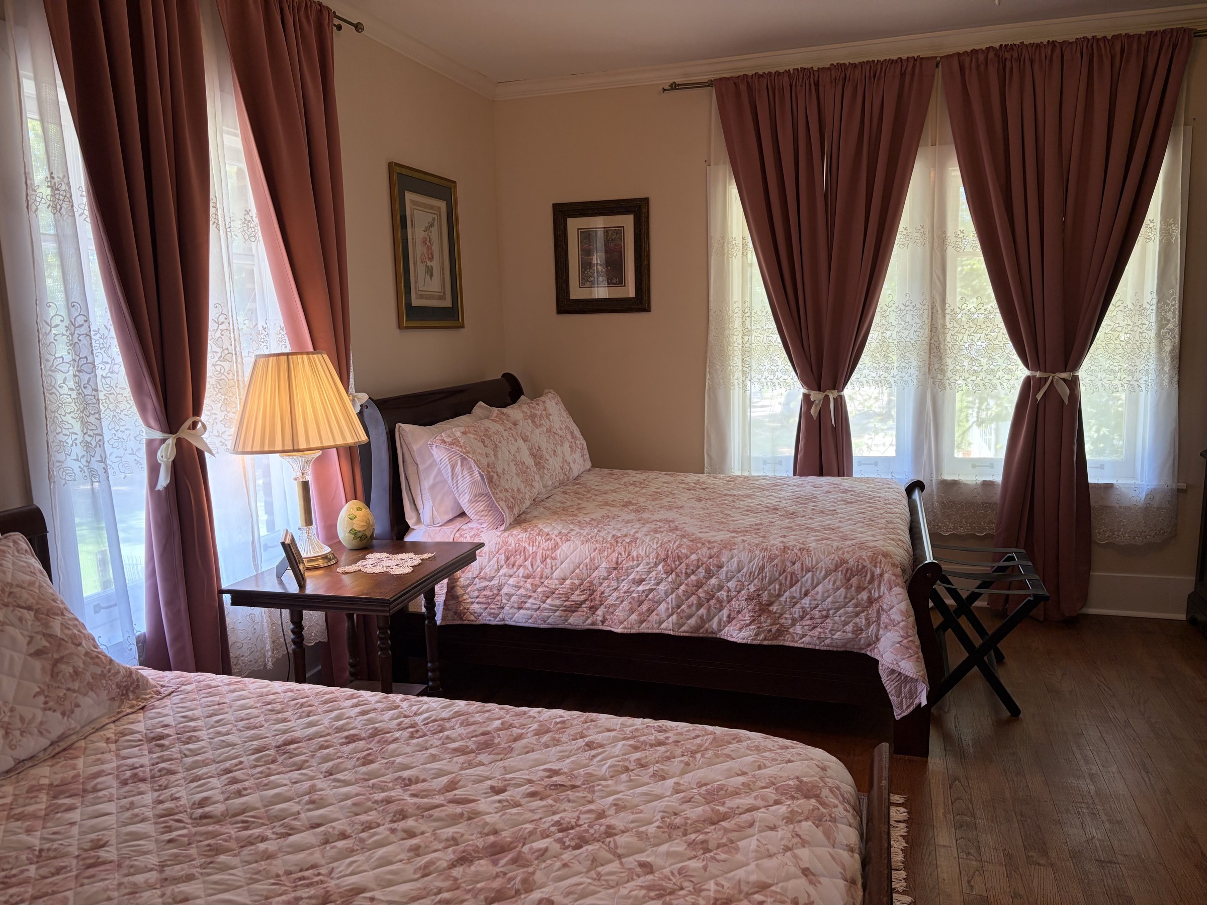 Margaret from the second bed, showing rose drapes, floral quilts, and a lamp on the nightstand.