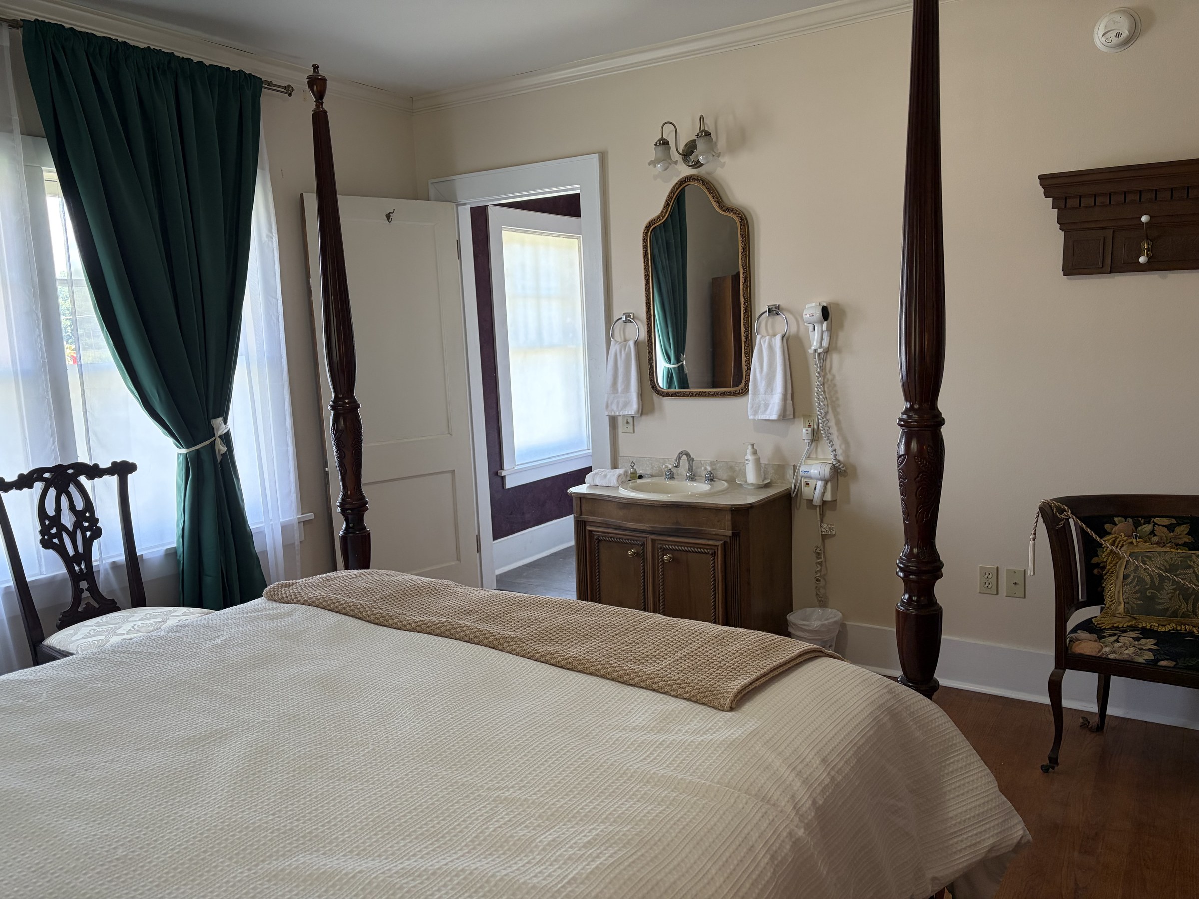 Mary looking toward the vanity and adjoining doorway, with green curtains and hardwood floors.