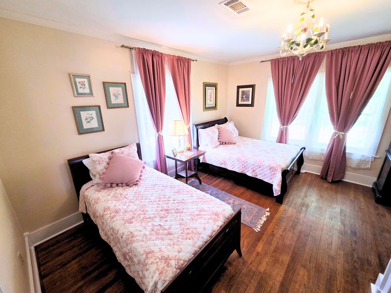Margaret: a full bed and a twin bed in dark wood with pink floral quilts, rose drapes, and a small flowered chandelier.