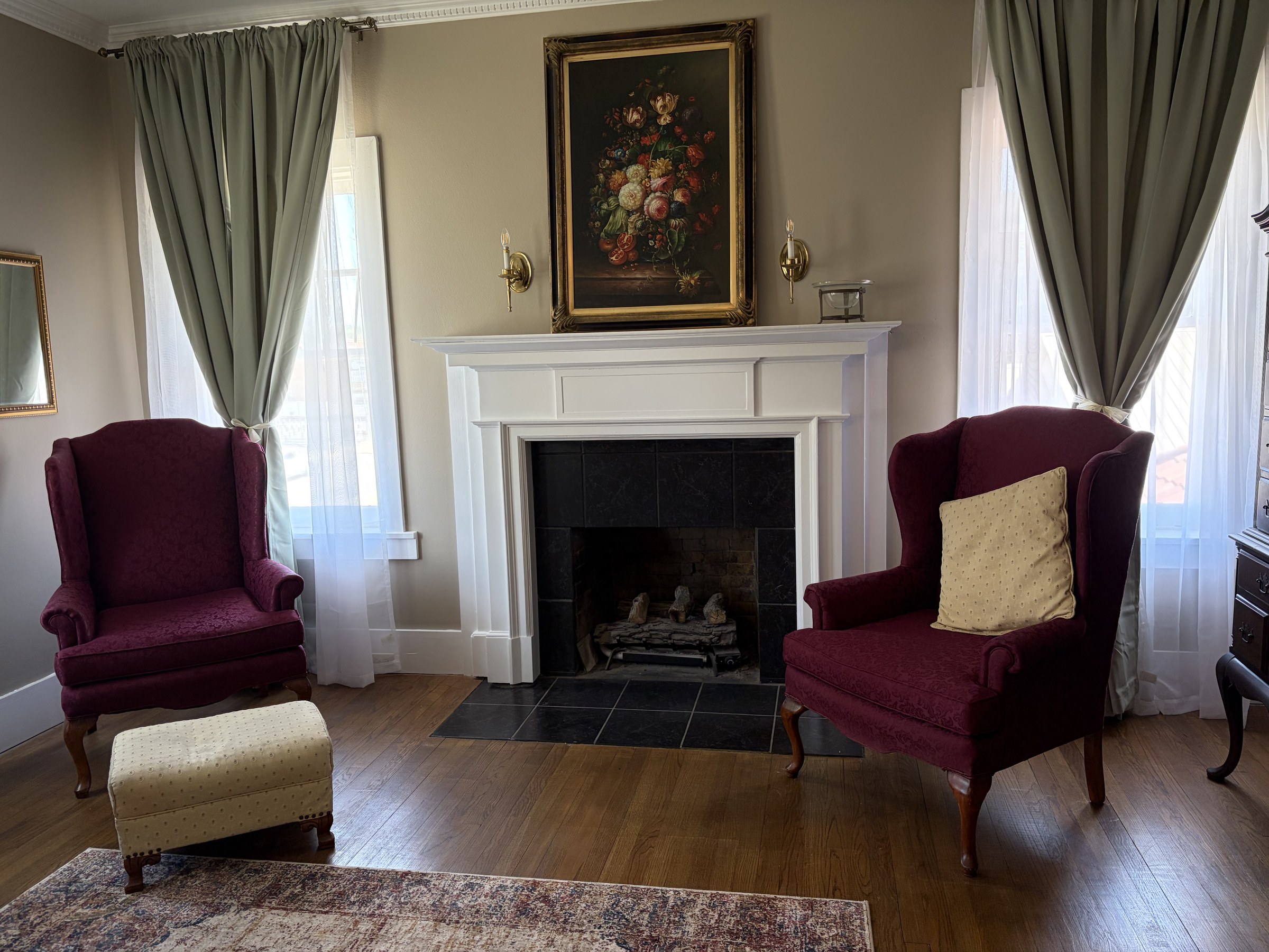 Thompson suite sitting area: white fireplace, burgundy wingback chairs, and sage drapes.