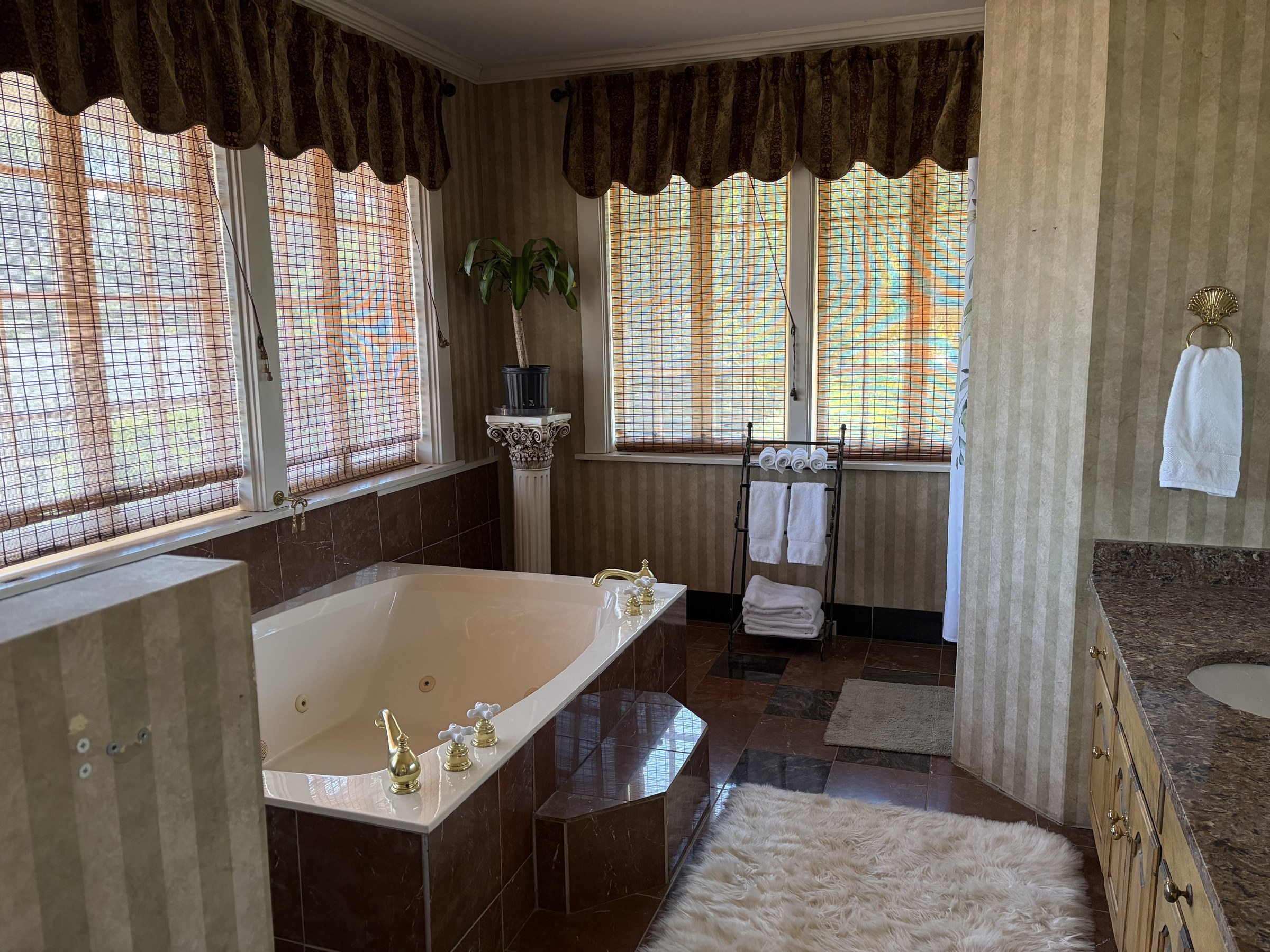 Thompson suite bath with a jetted soaking tub, gold fixtures, and striped wallpaper.